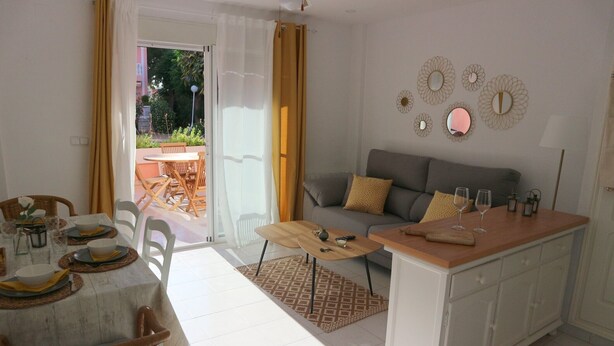 Un coin repas avec une table dressée pour deux personnes, un canapé et un espace cuisine doté d’un plan de travail.