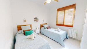 Une chambre avec deux lits, une fenêtre avec des stores, un radiateur et des éléments de décoration murale.