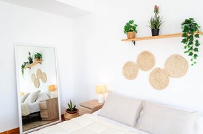 A bedroom with a bed, bedside table, lamp, mirror, and wall-mounted shelves with plants and woven placemats. - Villa "El Riu del Cel" with Private Garden, Private Pool, and Wi-Fi (Lloret de Mar)