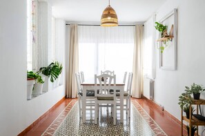 A dining area with a white table and chairs, a patterned floor, and a hanging light fixture. - Villa "El Riu del Cel" with Private Garden, Private Pool, and Wi-Fi (Lloret de Mar)