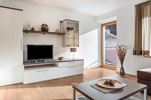 Un salon moderne avec un téléviseur à écran plat, une vitrine, une table à manger avec un set de table et un vase contenant des fleurs séchées.