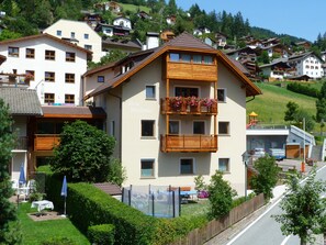 Un immeuble à plusieurs étages doté de balcons, une enseigne indiquant « Cesa Stefania », et une vue sur une colline où se trouvent d’autres bâtiments.