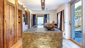 Un interior moderno con una isla de piedra, paredes de madera, vistas a través de una puerta de cristal y una lámpara colgante.