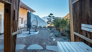 Una estructura de madera abierta con un sendero de grava, un banco, una mesa y una planta en maceta.