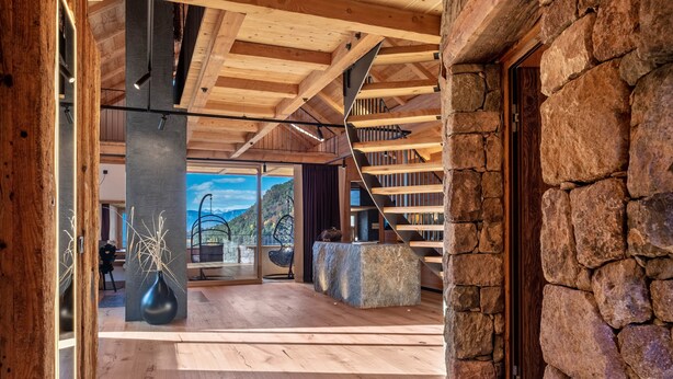 Un interior espacioso con techo de madera, paredes de piedra y vistas a un paisaje montañoso.