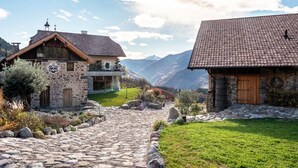 Un edificio de piedra con puerta de madera y pared de piedra, rodeado de un sendero de piedra y vegetación.