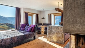 A bedroom with a large window, a bed, a dining table, and a stone accent piece. - Apartment "Spornberg Mountain Living Ostberg" with Mountain View (Renon)
