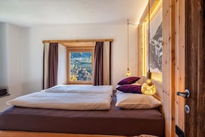 Ein Schlafzimmer mit einem großen Bett, einem Fenster mit Vorhängen, einer Holztür und einer wandmontierten Lampe.