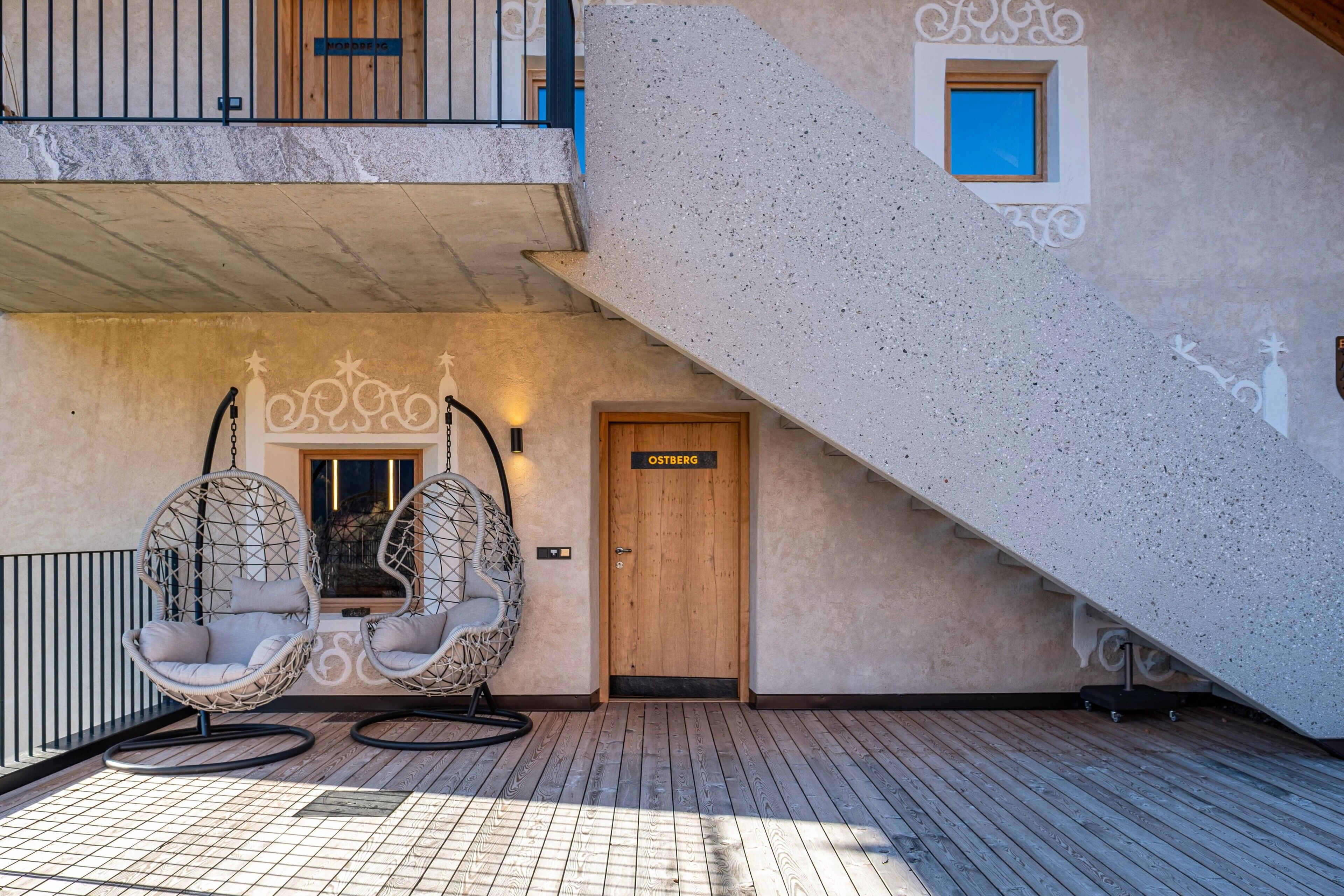 Eine Holztür mit der Aufschrift 'OSTBERG', ein Hängesessel und ein Balkon mit Geländer.