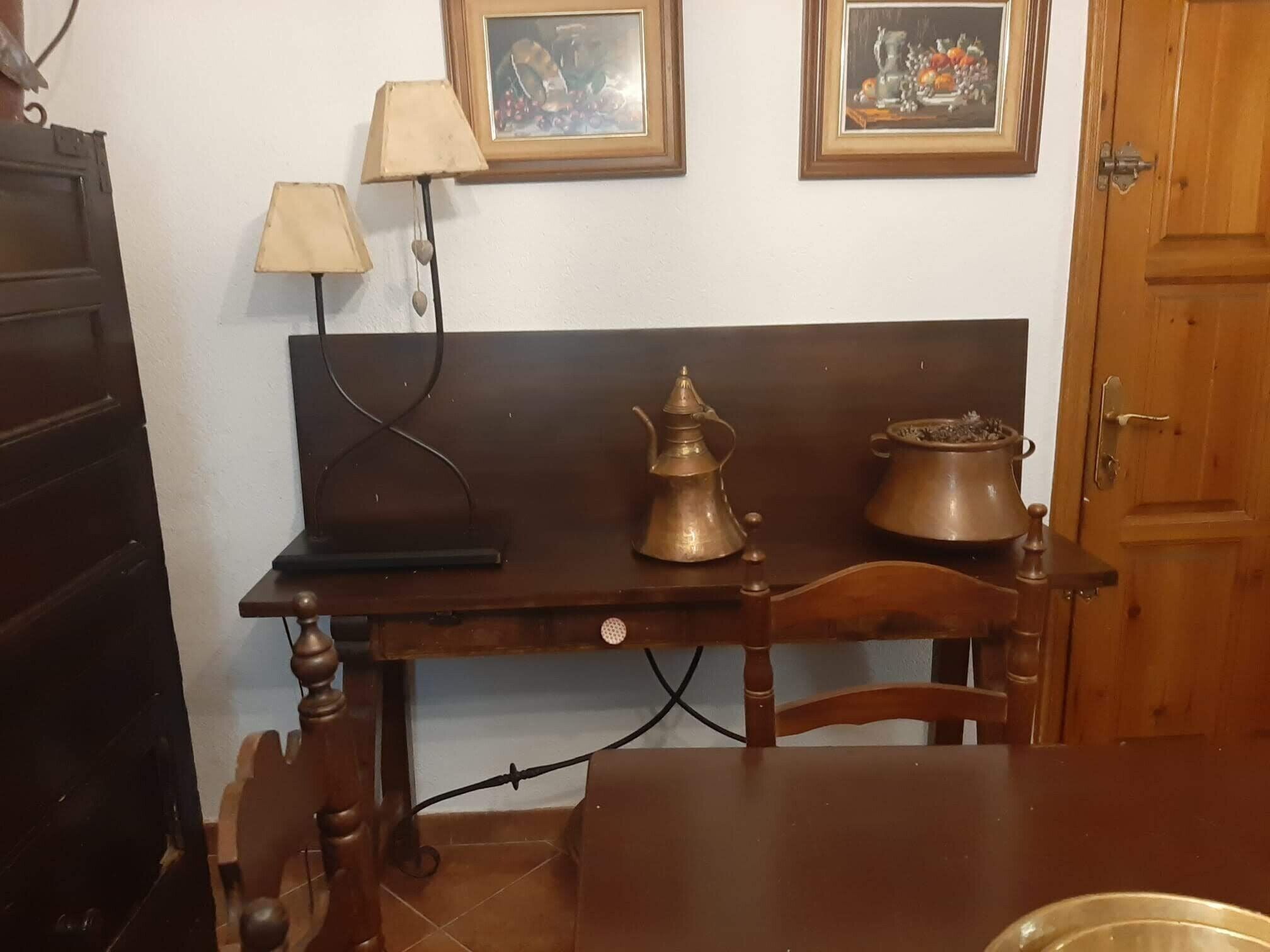 A wooden table with a lamp, a brass teapot, and a ceramic pot on a tiled floor.