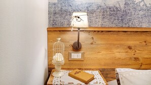 A wooden headboard with a wall-mounted lamp, a bedside table with a book and a decorative item, and a power outlet. - Holiday Apartment "Mantaula" with Mountain View, Shared Terrace & Wi-Fi (Teglio)