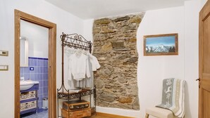 A room with a stone wall, a metal bed frame, a chair, a suitcase, and a painting. - Holiday Apartment "Mantaula" with Mountain View, Shared Terrace & Wi-Fi (Teglio)