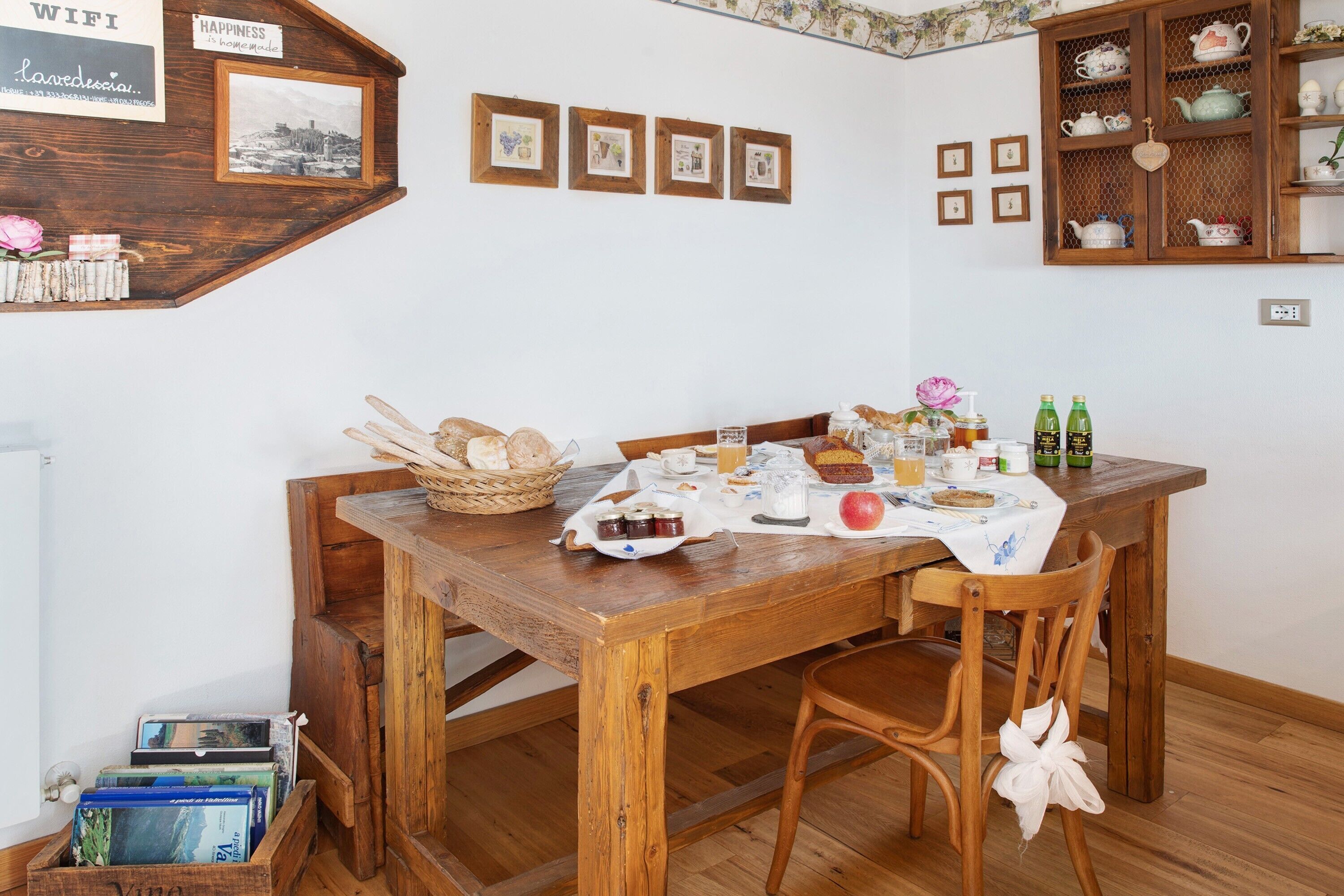 A wooden dining table with a white tablecloth, surrounded by chairs, in a room with a white wall and wooden cabinetry.