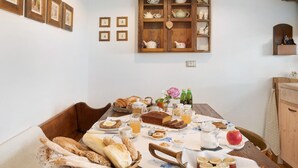 A dining table set with bread, pastries, and beverages, surrounded by chairs and a wicker basket. - Holiday Apartment "Mantaula" with Mountain View, Shared Terrace & Wi-Fi (Teglio)