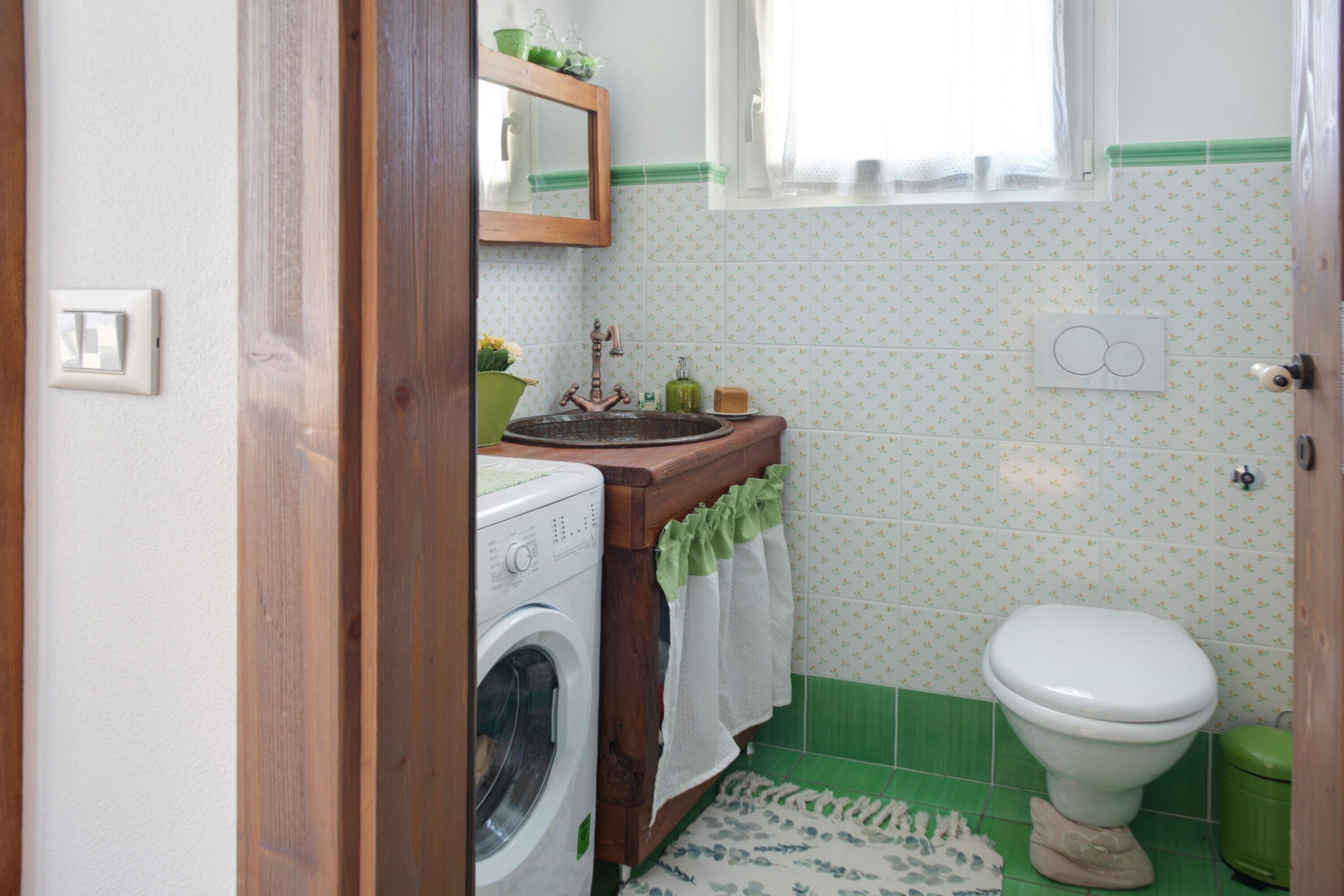 A bathroom with a washing machine, a sink with a mirror, a toilet, and patterned tiles.