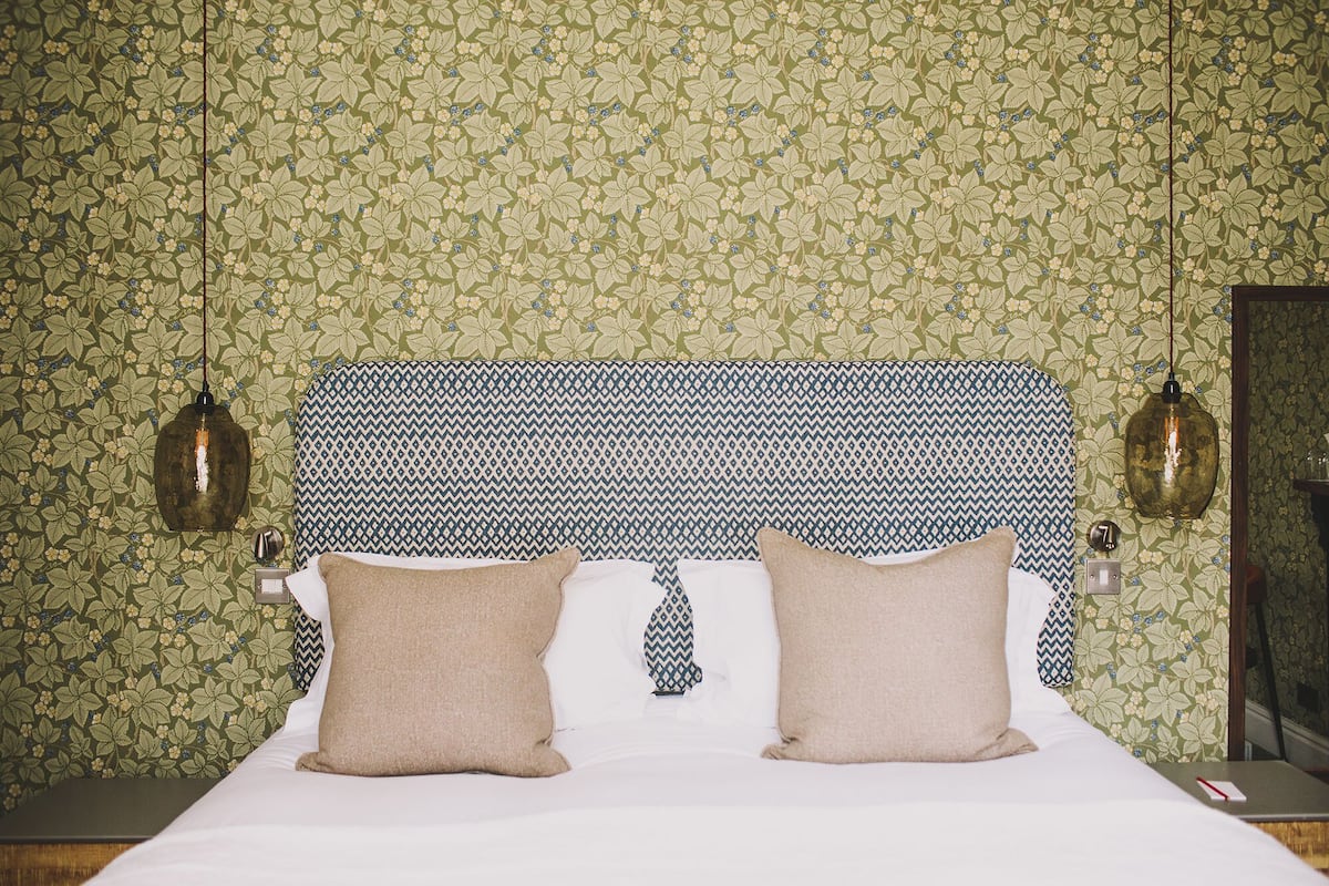 Una cama con dos almohadas, un cabecero estampado y dos lámparas fijadas a la pared.