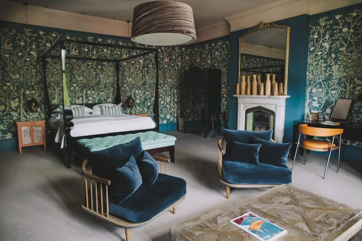 Un dormitorio con cama con dosel, una zona de estar con una silla y una mesita, y una chimenea.