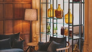 Una habitación acogedora con un muro de paneles de madera, una vitrina con botellas amarillas, un sofá azul y una lámpara.