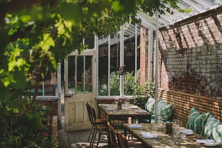 An outdoor patio with tables and benches, surrounded by greenery and brick walls.