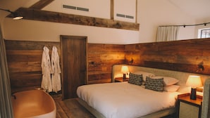 Un dormitorio con una cama grande, dos mesitas de noche con lámparas, un cabecero de madera, un banco de madera y un panel de pared de madera.