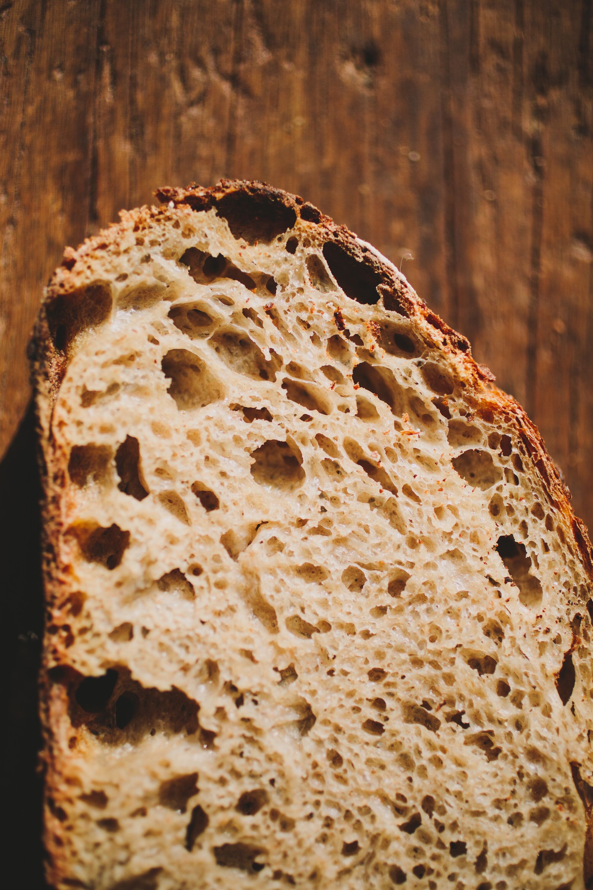 A slice of bread with a porous texture, placed on a wooden surface.