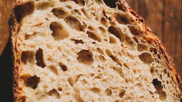 A slice of bread with a porous texture, placed on a wooden surface.