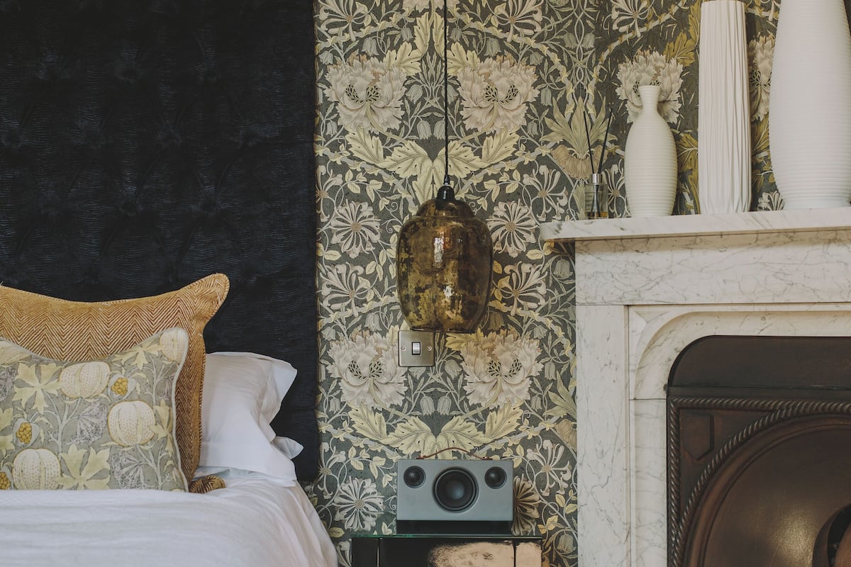Un dormitorio con cama, radio, chimenea y un papel tapiz floral.