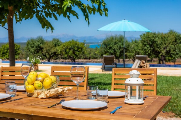 A wooden table set for dining outdoors with a bowl of lemons, wine glasses, and a lantern. - Finca "Can Jaumi" with Sea Views, Pool and Wi-Fi (Artà)