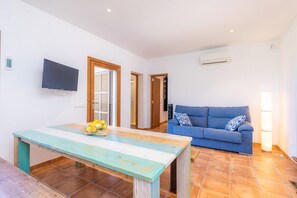 A living room with a blue sofa, a wooden table with fruit, a TV, and an air conditioning unit. - Finca "Can Jaumi" with Sea Views, Pool and Wi-Fi (Artà)