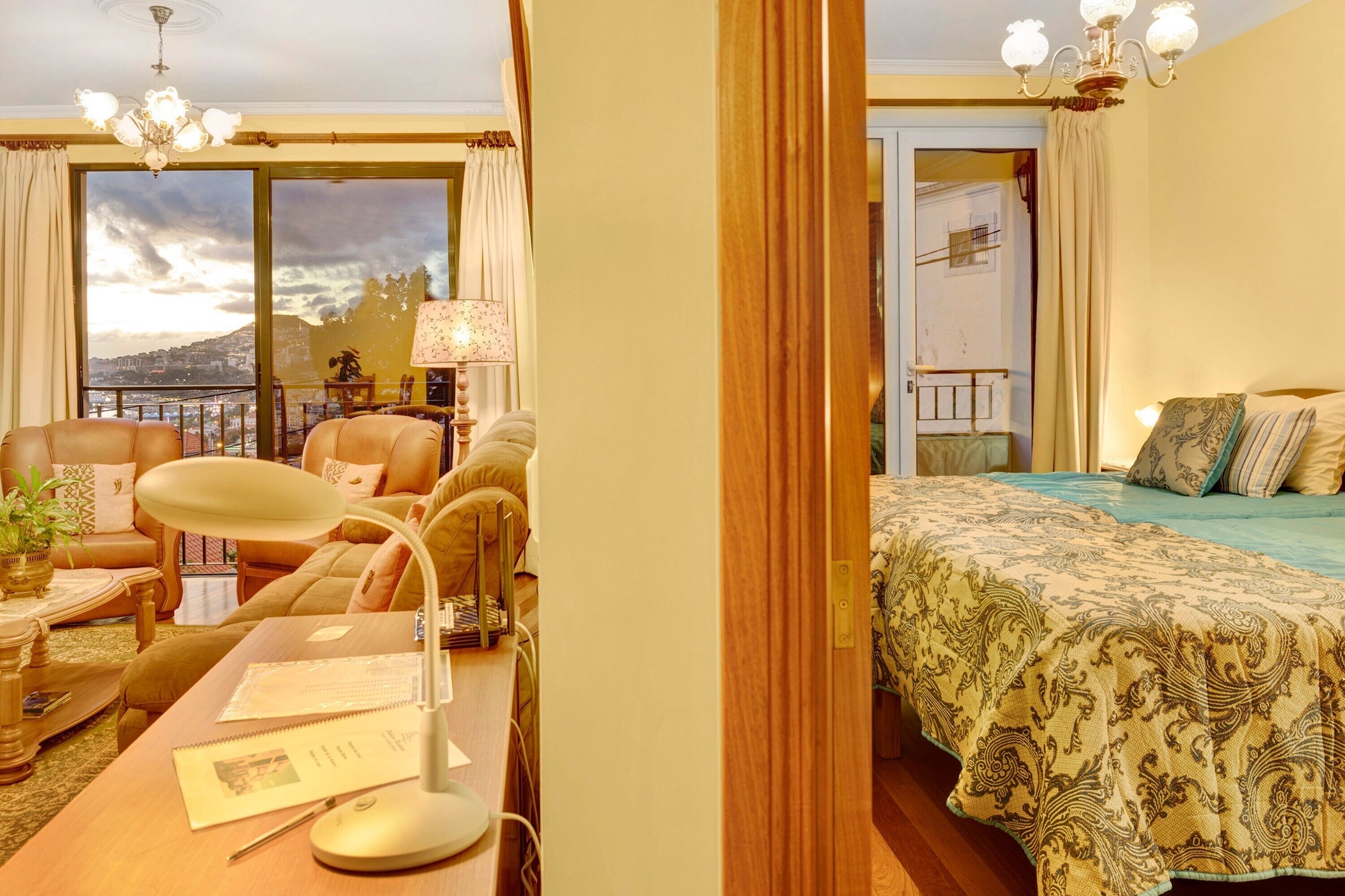 Habitación de hotel con escritorio, silla, lámpara y cama con ropa de cama estampada.