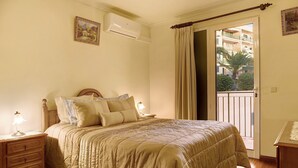 Una camera da letto con un letto, comodini, condizionatore d'aria, una finestra con tende e vista su un balcone.