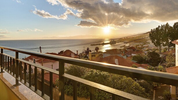 Un borgo costiero con vista sul mare, case dai tetti rossi e un cielo sereno con il sole al tramonto.