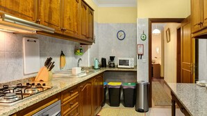 Una cucina con mobili in legno, un fornello a gas, un forno a microonde e bidoni per i rifiuti.