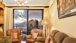 Un soggiorno con divano, due poltrone, una lampada, una pianta e un'ampia finestra con vista sulla città.