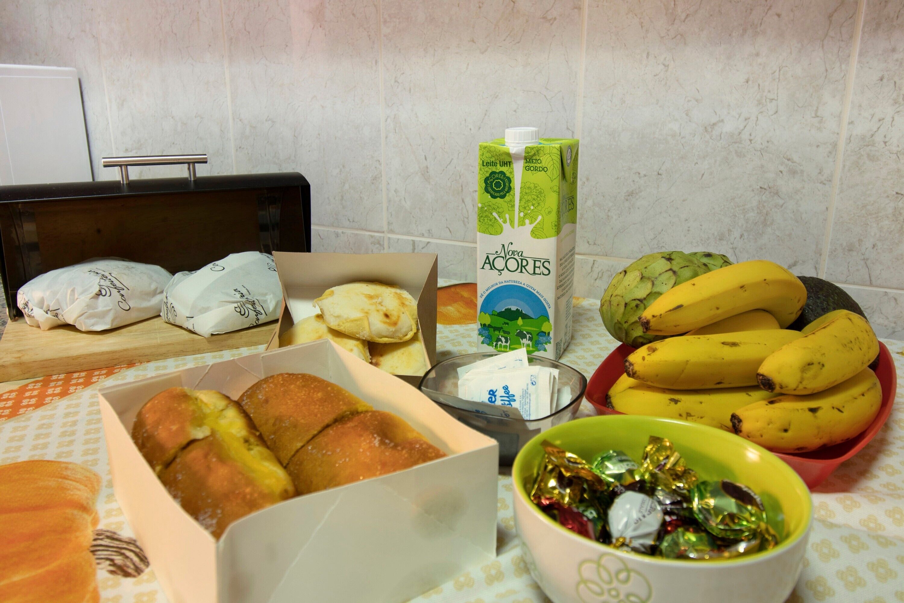 A kitchen counter with food items, including bread, a carton of milk, bananas, and a bowl of candies.