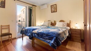 A bedroom with a bed, a chair, a nightstand, a dresser, a door, and a window. - Holiday Apartment "Palheiro Residence Familiar 1" with Sea View, Balconies & Wi-Fi (Funchal)