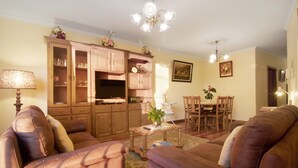 A living room with a sofa set, wooden cabinets, a dining table, and a chandelier. - Holiday Apartment "Palheiro Residence Familiar 1" with Sea View, Balconies & Wi-Fi (Funchal)