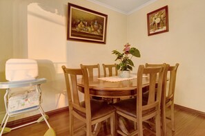 Une salle à manger avec une table ronde en bois, six chaises, une petite plante en pot et deux tableaux encadrés accrochés au mur.