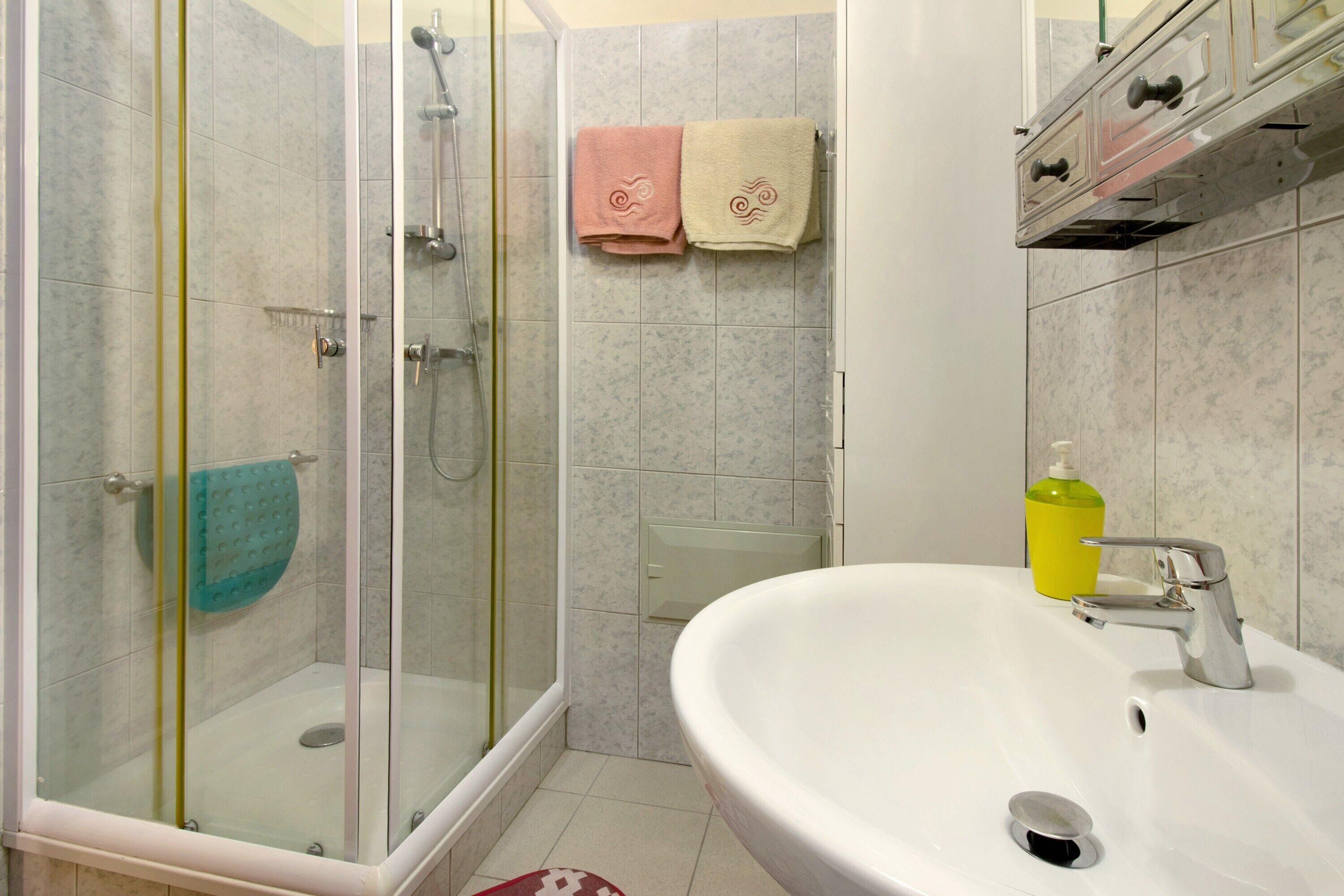 A bathroom with a glass-enclosed shower, a white sink with a chrome faucet, and two towels hanging on the wall.