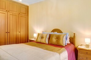 Une chambre à coucher avec un lit, une armoire en bois, des tables de chevet et des lampes.