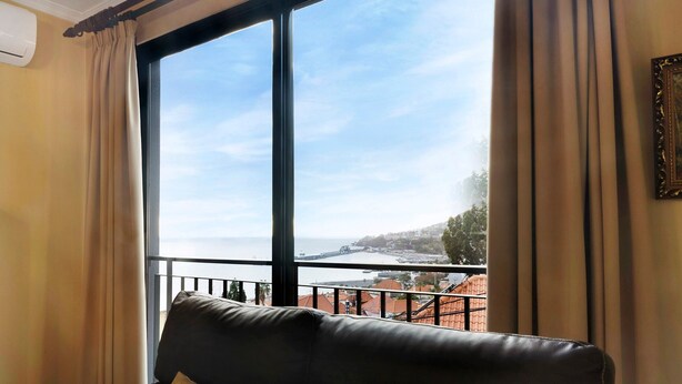 Een kamer met een groot raam, een leren bank en uitzicht op de kust.