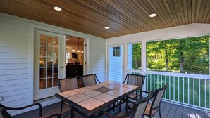 Une terrasse couverte avec une table et des chaises, une vue sur l’extérieur et une porte donnant sur un espace intérieur.