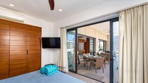 Habitación de hotel con cama, televisor y puerta corrediza de vidrio que da a un balcón con zona de comedor.
