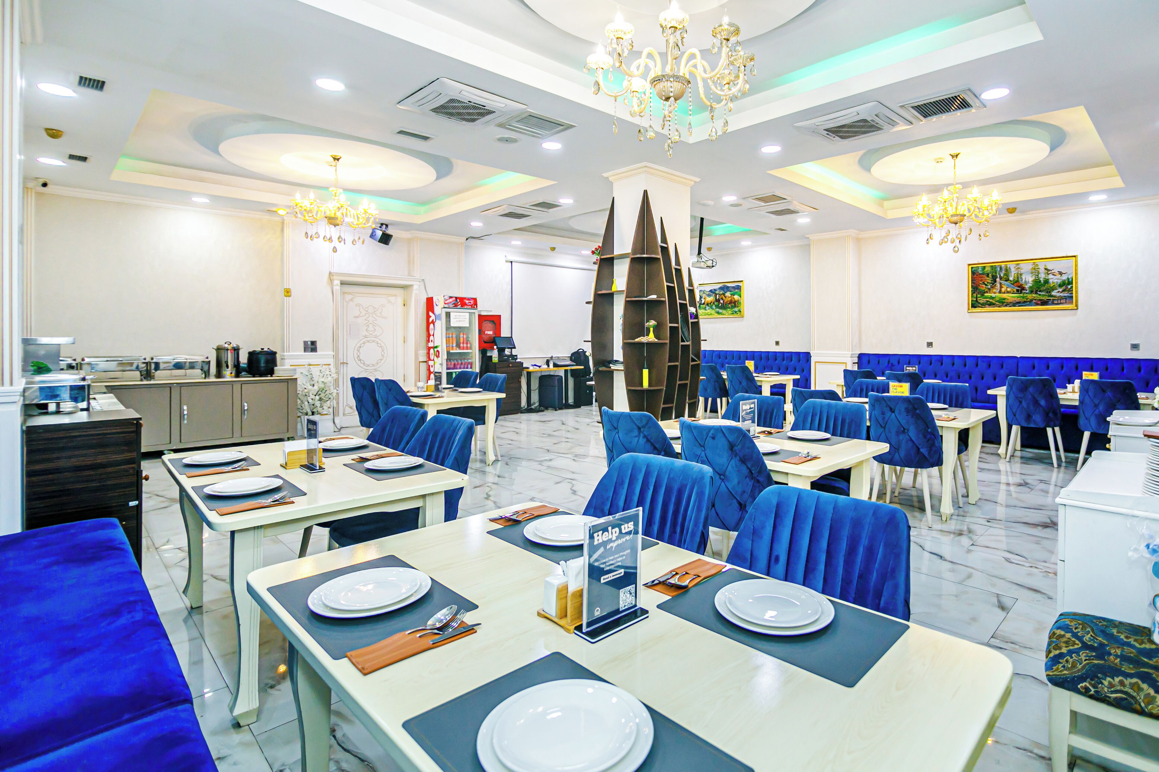 Een restaurant met blauwe gestoffeerde stoelen, witte tafels en kroonluchters.