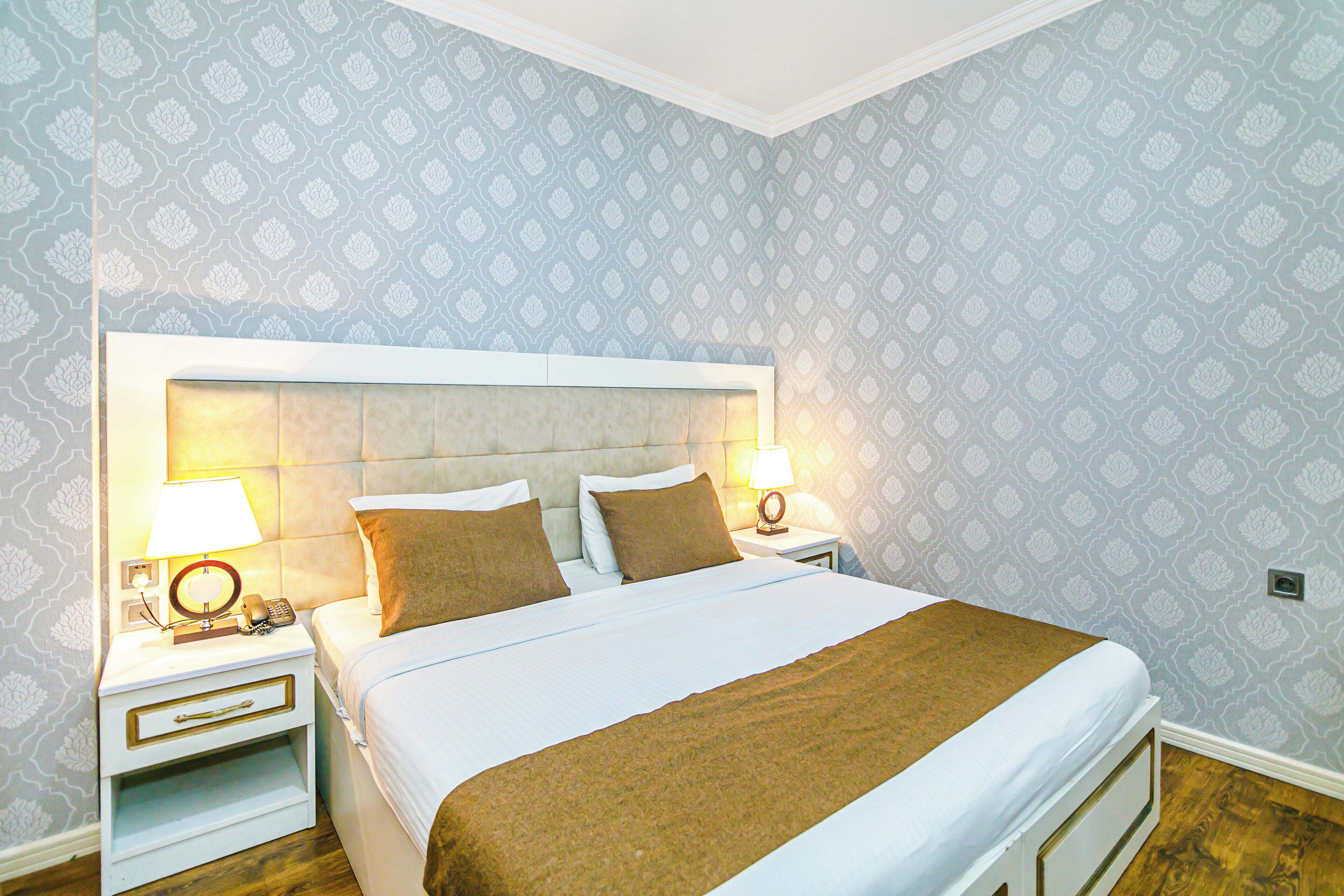 A neatly made bed with a brown throw, two bedside lamps, and a patterned wallpaper.