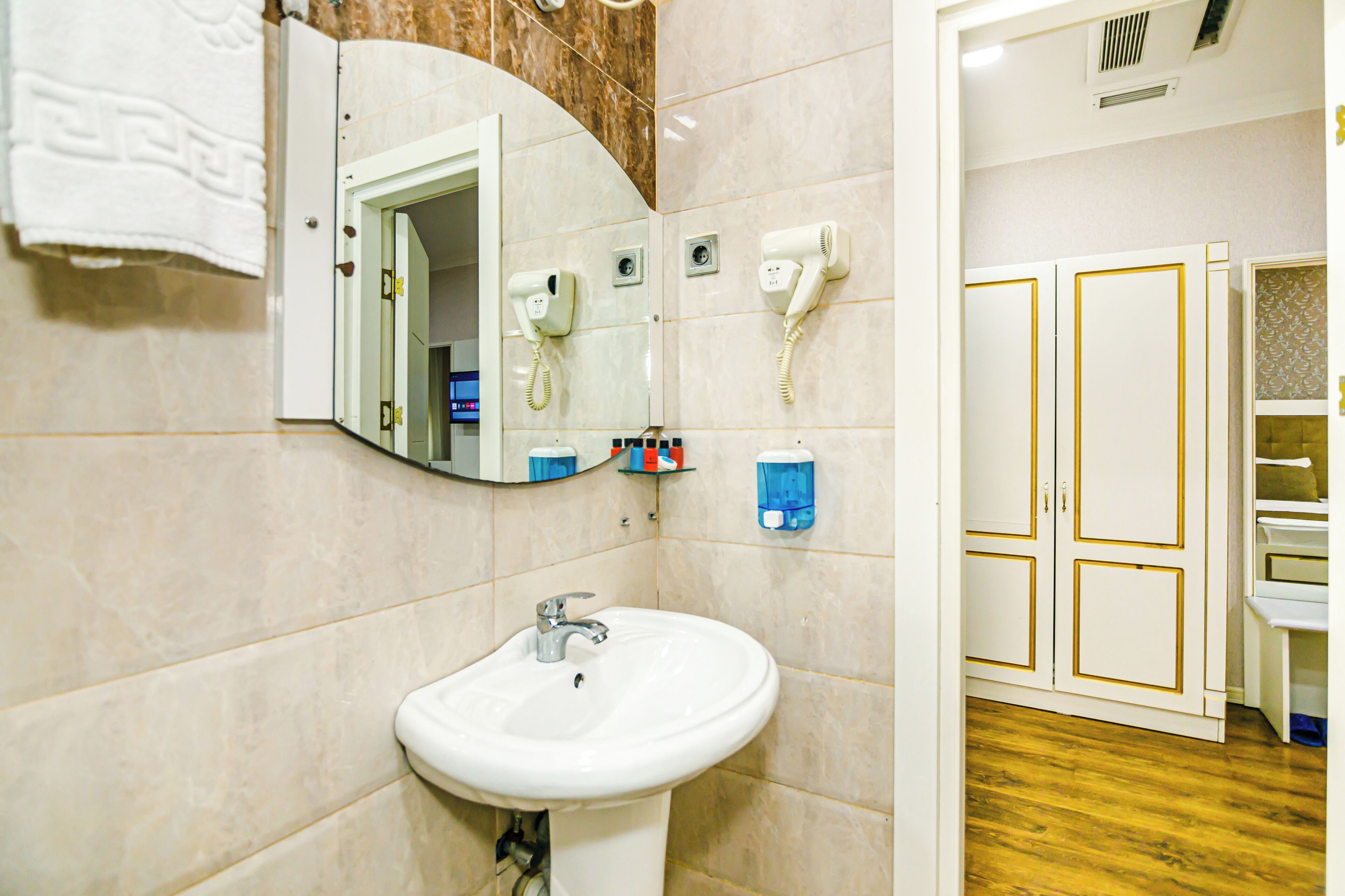 A bathroom with a white sink, a mirror, a hairdryer, and a towel hanging on the wall.