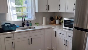 Ett modernt kök med vita skåp, ett kylskåp i rostfritt stål, en diskho med blandare och ett fönster med utsikt över grönområden utanför.