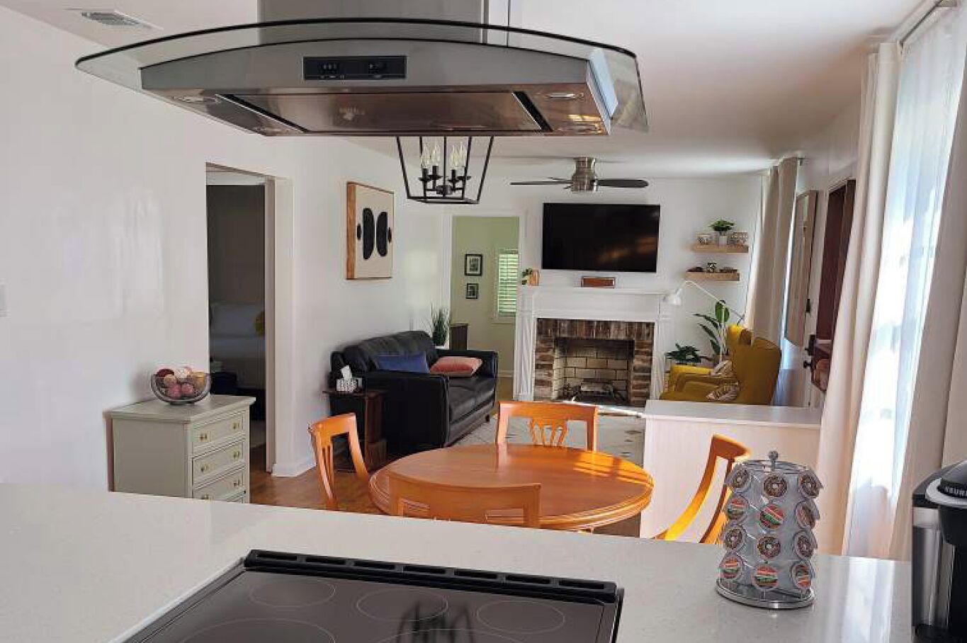 A modern kitchen with a central island, a dining area with a round table and chairs, a fireplace, and a living room with a sofa and a TV.