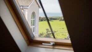 A view through a window of a house with a sloped roof and a grassy field in the background. - Old School Cottage Ship Farm Rhossili (Swansea)