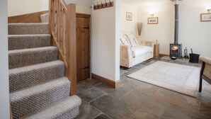 A staircase with carpeted steps, a wooden door, a wall-mounted coat rack, a sofa, a rug, and a wood-burning stove. - Old School Cottage Ship Farm Rhossili (Swansea)